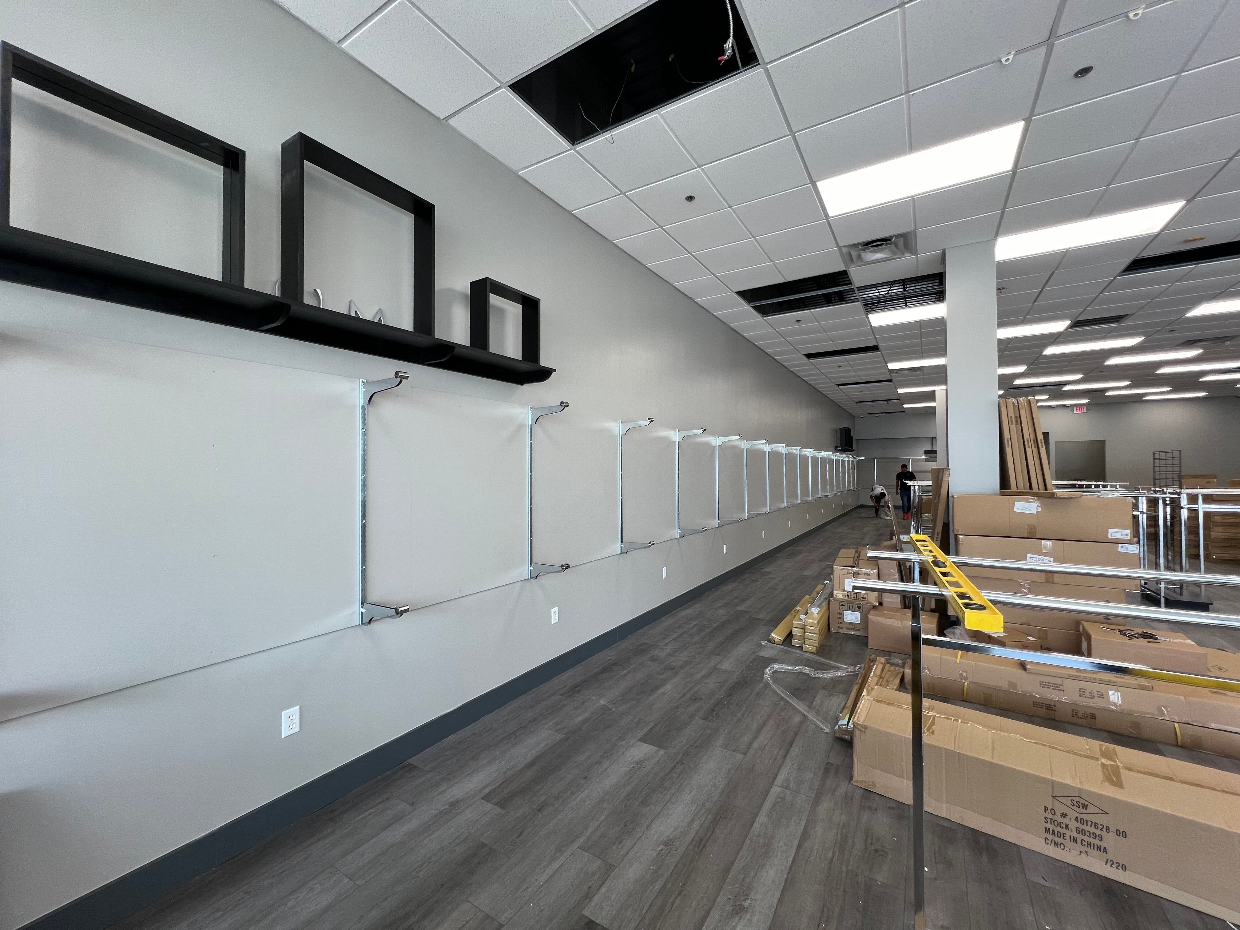 Long white wall with empty shelves and decorative frames, construction visible.