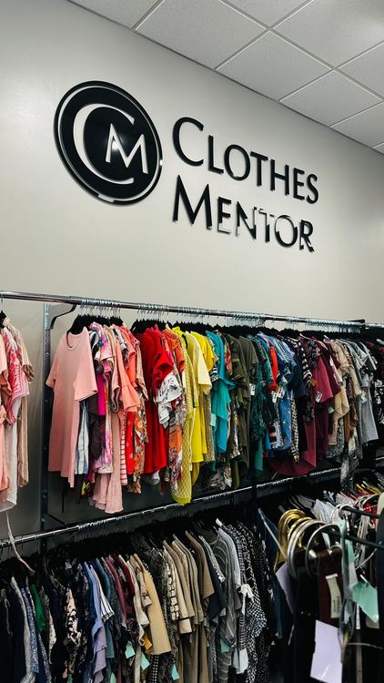 Inside a Clothes Mentor store, showcasing the brand logo and a wide selection of fashionable, pre-owned clothing on display.