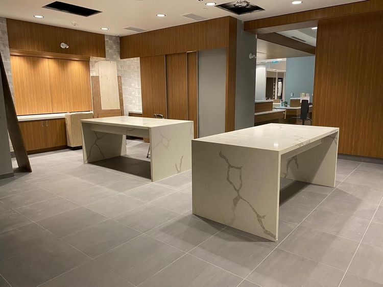 Two white quartz islands with elegant grey veining define a modern room with light wood cabinetry and grey tiled floors.