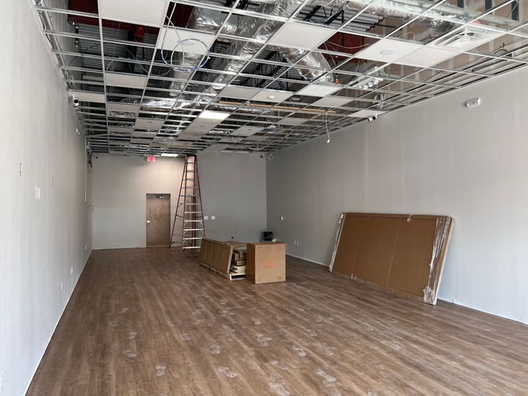 An empty commercial space features an exposed ceiling grid, new wooden flooring, and a ladder ready for finishing touches.