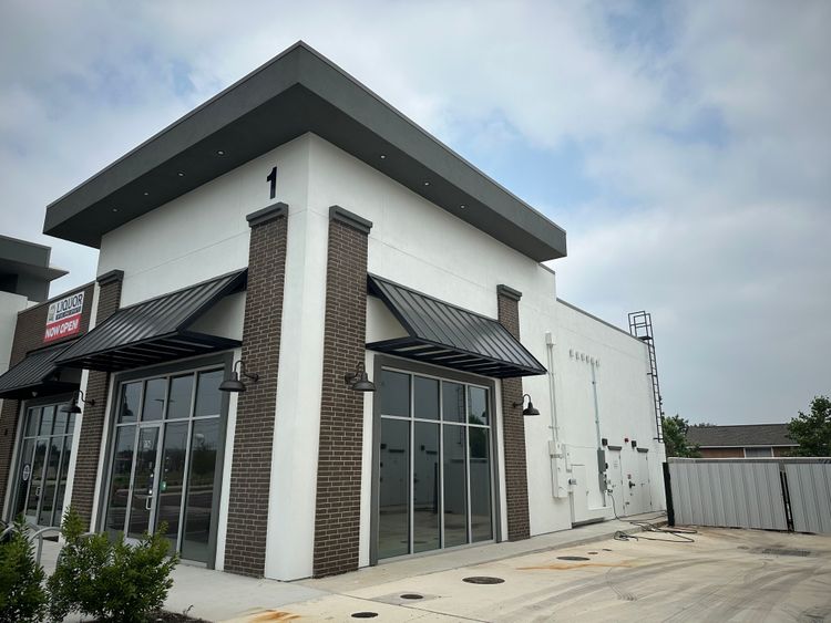 A modern commercial building exterior displays dark awnings, large windows, and a mix of white and brown finishes.