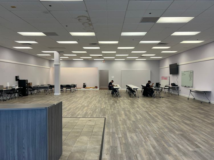 Two individuals are working at desks in a spacious, empty classroom or office setup.